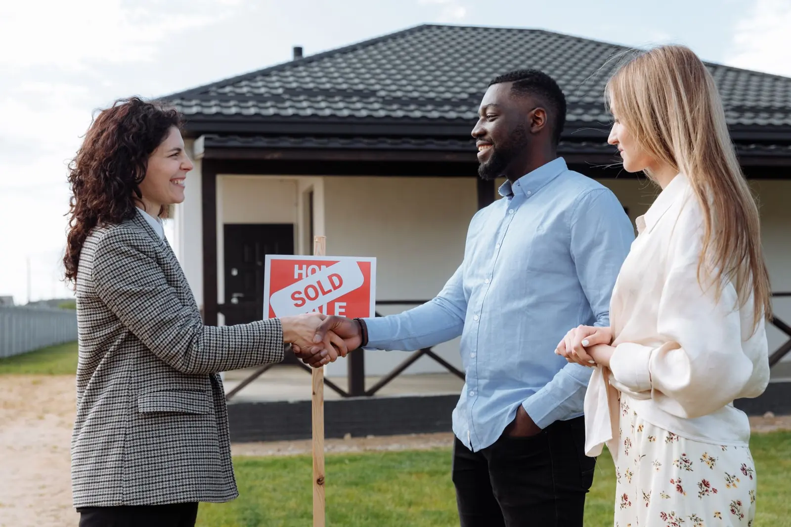 Couple with their agent in front of a newly purchased home