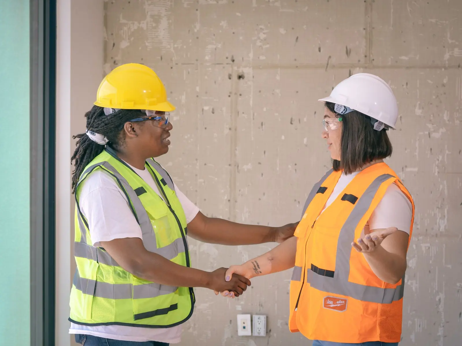 Two electricians in safety vests shaking hands on a job site
